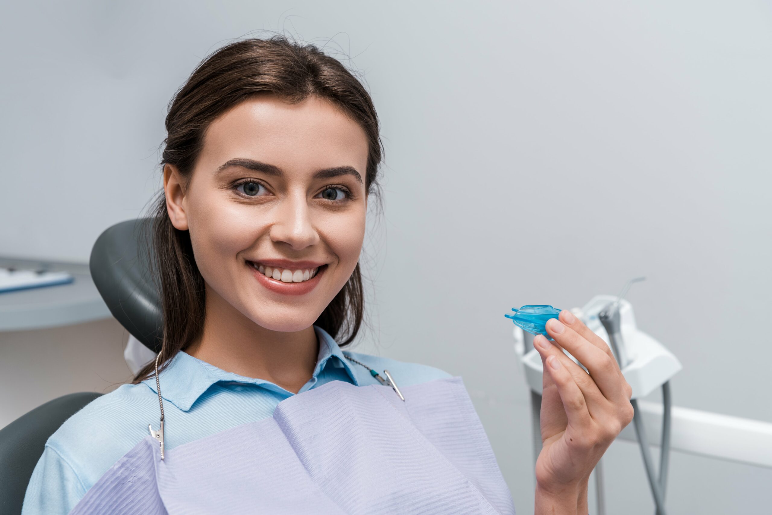 Cheerful woman holding blue retainer in dental clinic