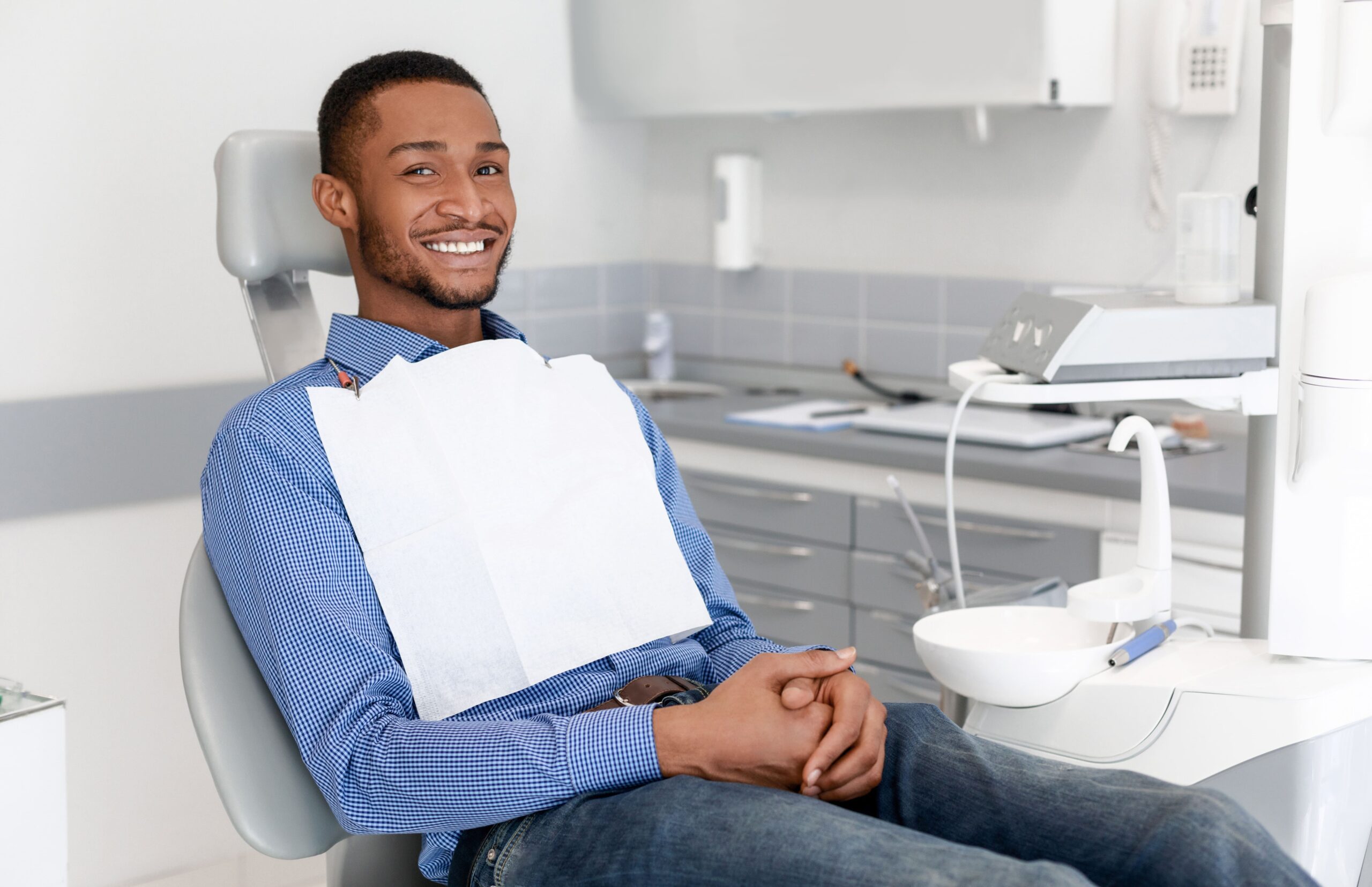 Happy black guy sitting on dentist chair and smiling at camera, attending dental clinic, copy space