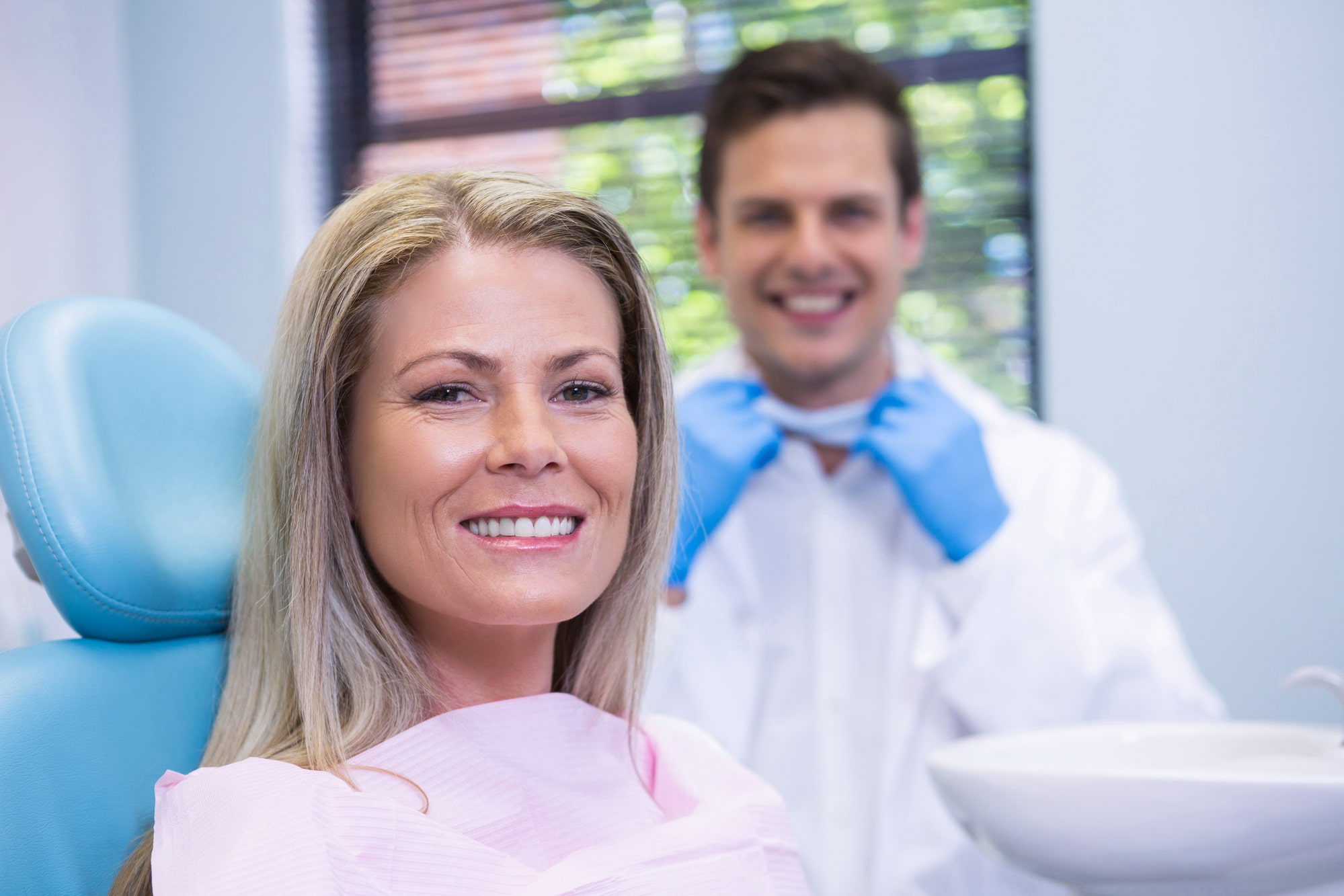 Portrait of smiling woman sitting on chair against dentist at medical clinic